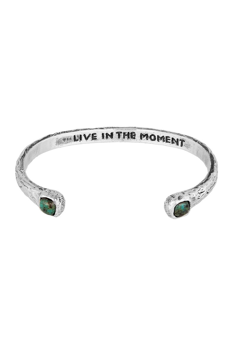 Silver cuff bracelet with a textured finish, featuring two turquoise stones at each end and an engraved phrase "LIVE IN THE MOMENT."