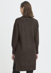 Hosszú barna kötött pulóver kerek nyakkivágással, bordázott mandzsettákkal és alsó szegéllyel. Oldalsó hasítékok a könnyű mozgásért. Puha textúra, finom fényű.