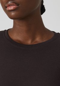 Tissu en coton côtelé foncé avec un col rond, présentant des détails de couture subtils et une texture lisse. Gros plan sur le tissu et le col.