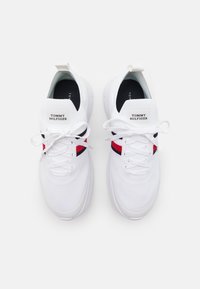 Bílé sportovní boty s síťovaným svrškem, šněrováním a štítkem Tommy Hilfiger. Na boku mají červené a námořnické pruhy. Gumová podešev.