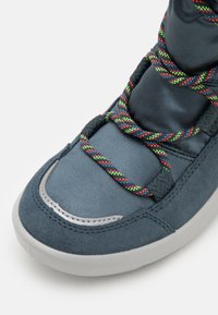 Šedé tenisky s hladkým textilním svrškem, semišovými akcenty, kovovým detailem a barevnými pletenými tkaničkami. Zaoblená gumová podrážka.