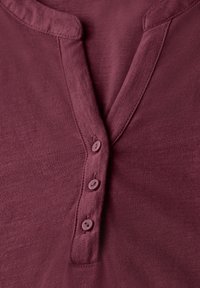 Mørkerød henley-skjorte med blødt stof, V-hals og fire knapper langs placket. Subtil tekstur med en afslappet pasform.