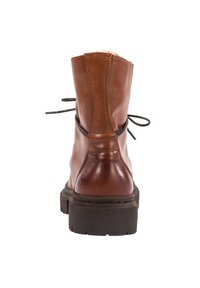 Bota de cuero marrón hasta el tobillo con un acabado suave, puntera redondeada, cierre de cordones y suela de goma negra texturizada. Vista trasera, acentos mínimos.
