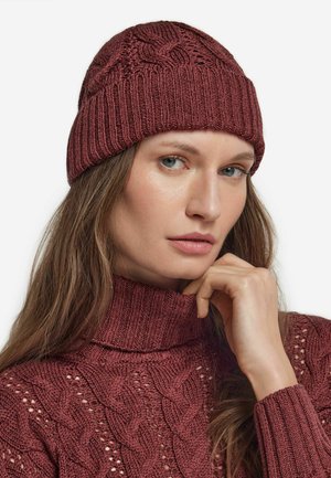 Bordeauxrode gebreide muts met een gestructureerd kabelpatroon en een geribde rand. Heeft een nauwsluitende stijl, gecombineerd met een bijpassende kabelgebreide coltrui.