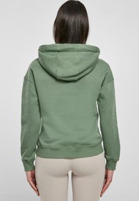 Sweatshirt à capuche verte avec une coupe décontractée. Doté de poignets et d'une taille côtelés, d'une texture douce et d'un design arrière sans coutures.