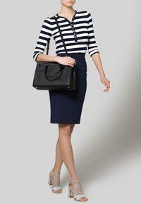 Sac fourre-tout noir, jupe crayon bleu marine et chemise rayée bleu marine et blanche avec des boutons. Talons transparents avec des brides à la cheville. Design simple et structuré.