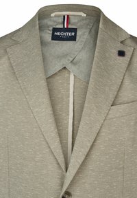 Helle beigefarbene Blazer mit einem strukturierten Stoff, mitreissenden Revers und einem dezent gemusterten Futter. Verfügt über eine Logospange und eine einzelne Brusttasche.