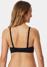 Zwarte bralette met verstelbare bandjes, een gladde stoftextuur en een drievoudige haaksluiting aan de achterzijde. Eenvoudig ontwerp zonder versieringen.