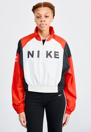 Nike īsa jaka ar baltu korpusu, sarkaniem un melniem piedurkņiem, augstu apkakli un izteiksmīgu melnu logotipu. Elastīga josta un aproces.
