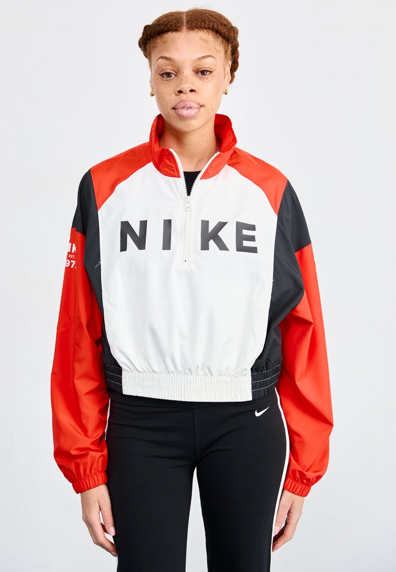 Nike īsa jaka ar baltu korpusu, sarkaniem un melniem piedurkņiem, augstu apkakli un izteiksmīgu melnu logotipu. Elastīga josta un aproces.