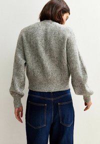 Maglione grigio a maglia con un design cropped e orlo a coste, caratterizzato da maniche ampie. Abbinato a jeans in denim blu scuro, mostrando dettagli posteriori.