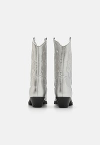 Botas de cowboy plateadas con detalles en costura. Punta afilada y tacón en bloque. Acabado metálico suave con acentos recortados en la parte superior.