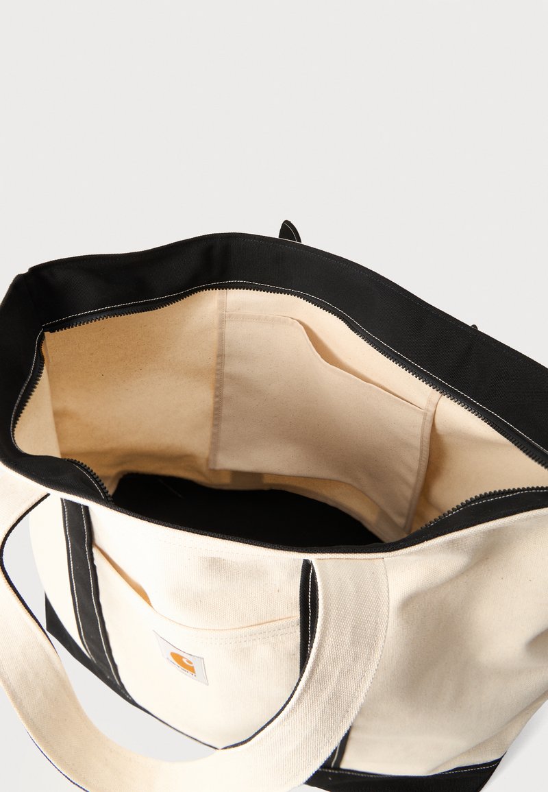 Canvas tote bag with black trim, beige interior, and open zipper, showing an inner pocket and sturdy handles.