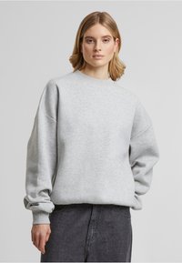 Grå sweatshirt med rund halsudskæring, dropped shoulders og ribstrikkede manchetter. Blød tekstur, oversized pasform, parret med en mørk nederdel.