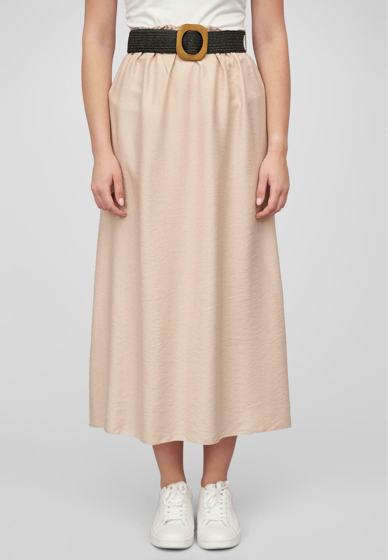 Longue jupe beige en tissu texturé, avec une taille froncée et une ceinture tissée noire ornée d'une grande boucle en bois rectangulaire. Associée à des baskets blanches.