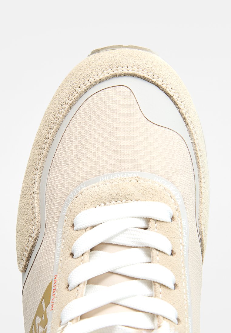 Scarpa sportiva beige con tomaia in suede testurizzato, accenti sintetici lisci, lacci bianchi e un logo discreto vicino alla punta.