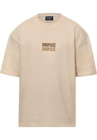 Beige katoenen t-shirt met korte mouwen, een ronde halslijn, en een vooropdruk van het woord "DROPSIZE" in verschillende bruin tinten.
