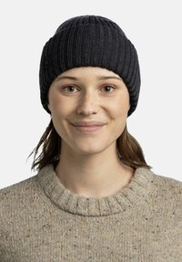 Knit beanie in dark gray with ribbed texture. Light brown sweater with speckles and a high ribbed collar. Close-up portrait of a person.