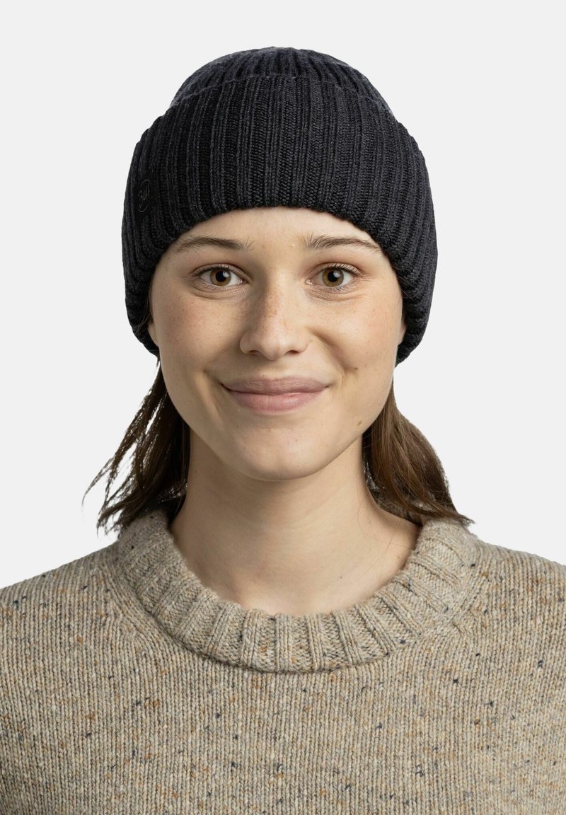 Knit beanie in dark gray with ribbed texture. Light brown sweater with speckles and a high ribbed collar. Close-up portrait of a person.