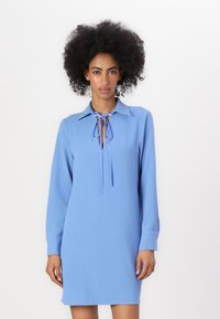 Abito blu con collo, maniche lunghe e chiusura a cravatta al collo. Tessuto morbido con una vestibilità rilassata, che termina appena sopra il ginocchio.