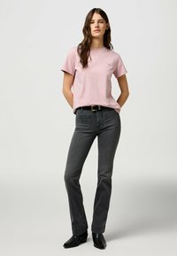 Lyserød bomulds T-shirt med korte ærmer, prydet med et lille logo. Kombinationen med grå denimjeans, accentueret af et sort bælte og støvler.