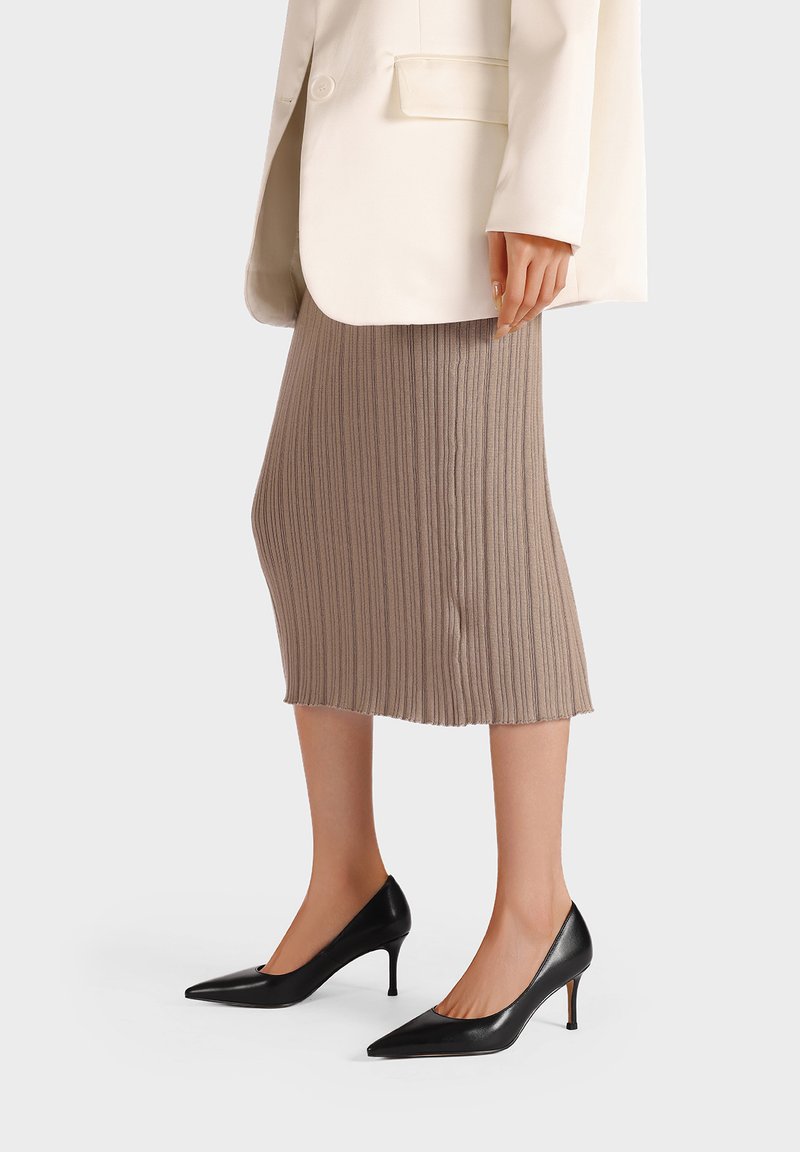 Gonna midi plissettata beige abbinata a un blazer bianco e tacchi a punta nera, che mettono in risalto texture morbide e linee sartoriali.