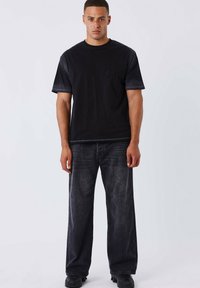 Camiseta de algodón negra con un diseño texturizado en el pecho, combinada con jeans de mezclilla oscuros y texturizados y zapatillas negras.