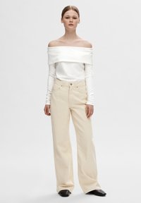 Off-shoulder hvit topp med lange ermer, kombinert med beige vide bukser og svarte spisse sko. Enkelt design, glatt tekstur.