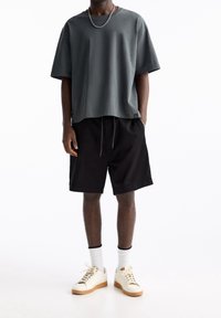T-shirt gris à manches courtes, coupe décontractée, avec un short noir et des baskets crème. Comprend une chaîne argentée et des chaussettes blanches avec des accents noirs.