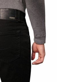 Czarne dżinsy z widocznym przeszyciem, skórzany pas z logo "PIONEER", w komplecie z szarym swetrem z długim rękawem, na którym częściowo widać rękę.