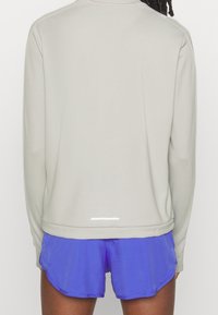 Haut à manches longues gris clair avec une coupe décontractée, doté d'une bande réfléchissante à l'arrière, associé à un short de sport bleu vif.
