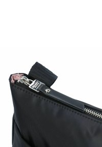 Esquina de una bolsa de nylon negra con un zipper plateado, tirador de cuero y forro interior rosa. Presenta una correa texturizada para un mejor agarre.