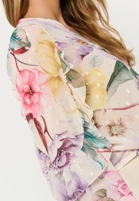 Kimono floreale in chiffon leggero con maniche arricciate, caratterizzato da grandi fiori rosa, gialli e viola. Decorato con dettagli metallici.