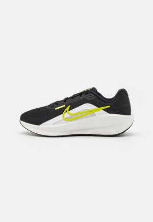 Czarno-biały but do biegania Nike z neonowo-żółwym logo, oddychającą siateczkową cholewką i miękką białą podeszwą na jednolitym tle.