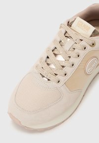 Beige sneaker met een bovenwerk van mesh en suède, ronde neus, reflecterende accenten en gestructureerde veters. Heeft een logo-label aan de zijkant.