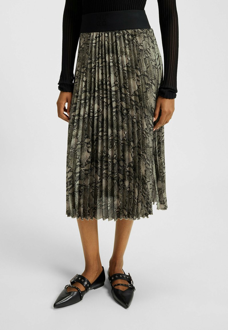 Plisowana spódnica w zielono-czarny wzór węża, z szerokim czarnym pasem w talii. W połączeniu z czarnymi czółenkami na spiczastym obcasie i ozdobnymi paskami.