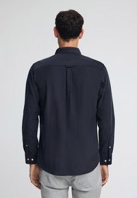 Camicia blu scuro con maniche lunghe, realizzata in un tessuto liscio. Presenta un colletto classico, dettaglio del yoke posteriore e polsini con bottoni.