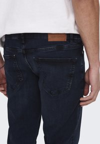 Mörkblå denimjeans med en figurnära passform, med en läderetikett på baksidan av midjan och två bakfickor med sömdekoration.