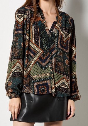 Kobieta w bluzce z długim rękawem w stylu patchwork z dekoltem w szpic oraz ciemnozielonej skórzanej mini spódniczce.