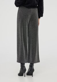 Pantaloni neri e argento a gamba larga con vita alta, caratterizzati da un tessuto liscio e da un leggero luccichio, abbinati a stivali neri con tacco.