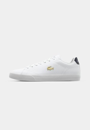 Zapatilla blanca con parte superior de cuero liso, acento del logo dorado en el costado y suela de goma texturizada. Presenta una lengüeta azul en el talón.