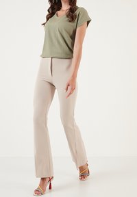 Top verde chiaro a maniche corte con texture a coste, abbinato a pantaloni beige a campana. Modella che indossa sandali con cinturini multicolori.