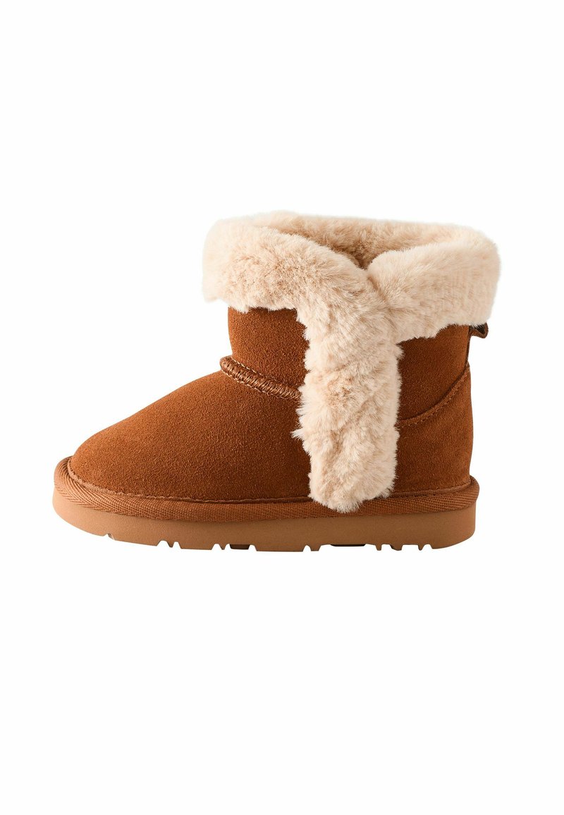 Brune ruskinds ankelstøvle med en blød beige faux-fur krave. Rund tå, flad sål og enkle syninger langs sømmene.