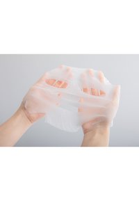 Maschera facciale bianca e leggera tenuta da due mani, con aperture a fessura per occhi e bocca, realizzata in materiale sottile e testurizzato.