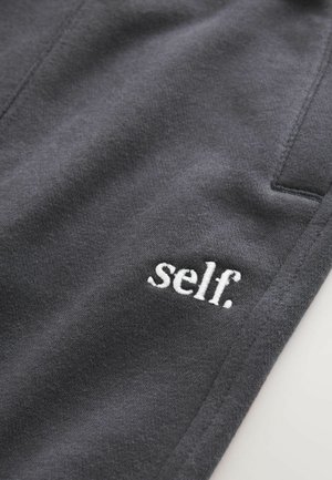 Hallid hallid joggers, millel on väike valge broderitud "self." logo, sujuva tekstuuri ja minimalistliku disainiga.