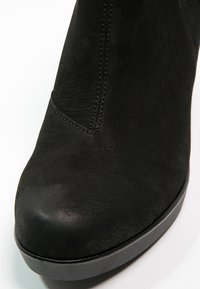 Gros plan d'une bottine en daim noir avec un bout arrondi et une couture verticale visible sur la partie supérieure.