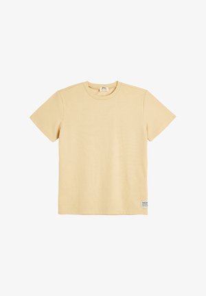 Beige kortærmet t-shirt lavet af ribbet stof. Har en rund halsudskæring og et lille mærke nederst til venstre med brandinformation.