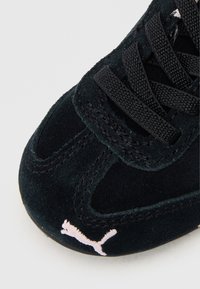 Černé semišové tenisky s texturovaným svrškem, černými tkaničkami, růžovým vyšitým logem na špičce a vyztuženými švy.