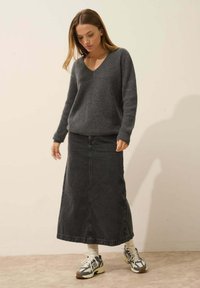 Szary sweter dziany z dekoltem w kształcie V, w połączeniu z długą czarną spódnicą dżinsową. Model nosi sneakersy w stonowanych kolorach i żebrowane skarpety.