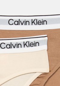 Beige és világosbarna Calvin Klein alsónemű szett, puha pamut anyagból készült, rugalmas derékrészekkel, amelyek szürke és fekete márkázással rendelkeznek.